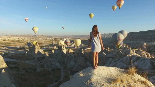 Woman Walking to Edge of Rock and Looking at Hot Air Balloons, Cappadocia, Turkey.