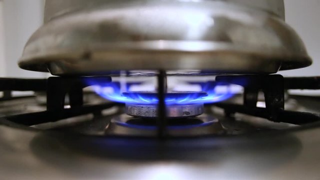 Silber kettle boiling on a gas stove. Denger on the kitchen; blue gas fire