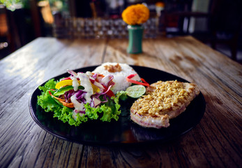 Grilled tuna steak with rice and vegetables in interior of a cafe.