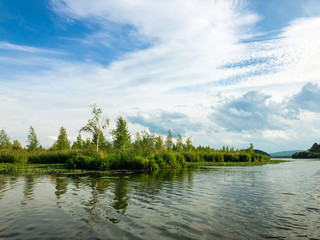 View of the lake and Islands with trees and vegetation. Cirrus and Cumulus clouds in the sky. A light breeze is blowing.