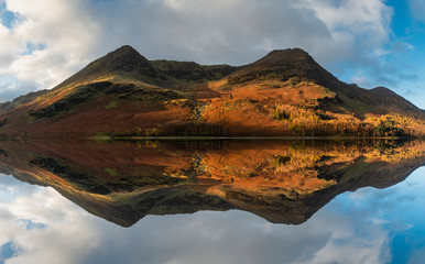 Majestic vibrant Autumn Fall landscape Buttermere in Lake District with beautiful early morning sunlight playing across the hills and mountains