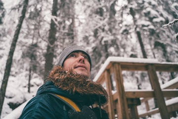 Photo of man in winter forest on wooden bridge.