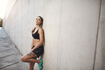 Sports, workout and healthy, active lifestyle concept. Attractive female athelete, sportswoman in activewear, resting, lean concrete wall looking camera after productive jogging exercise