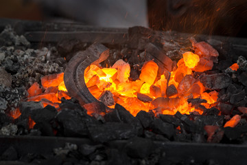 Horseshoe heating for forging. Embers glow in a iron forge. Fire, heat, coal and ash with flying sparks.