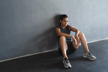 Fototapeta na wymiar Side-angle shot sassy good-looking, motivated athletic strong sportswoman in activewear, taking rest after workout, lean on gym wall, sit floor, waiting fitness instructor start functional training