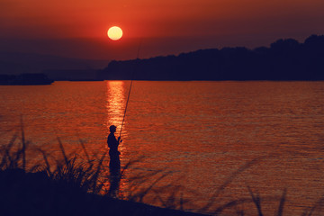 Silhouette of fisherman fishing on river at dusk.