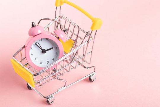 Small pink alarm clock in a shopping cart on a pink background - Powered by Adobe