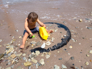 Little boy playing on the beach by the sea. He holds in his hands a yellow toy ship and green shoulder blade