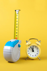 Measuring tape and alarm clock isolated over yellow bakground. Carpenter and Construct concept.