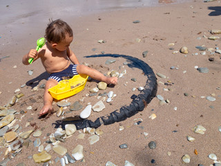Little boy playing on the beach by the sea. He holds in his hands a yellow toy ship and green shoulder blade