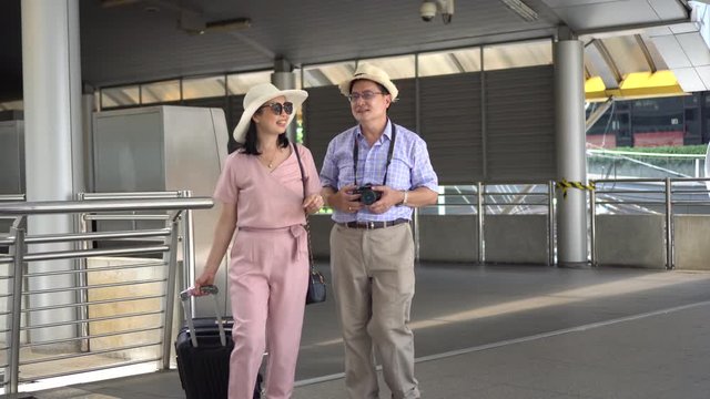 happy asian Senior couple tourists traveling walking with luggage in airport terminal . old man Travellers with camera taking a photo. elderly woman carrying suitcase. vacation. ageing society concept