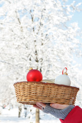 Woman's hand with christmas balls in a wicker basket at the winter park.