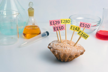 Food laboratory, cupcake decorated with nameplates of additives E, with close-up on a white table.