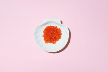 Porcelain plate with red caviar on a pink background