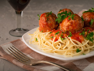 Cooked spaghetti and meatballs on a plastered background with a glass of wine