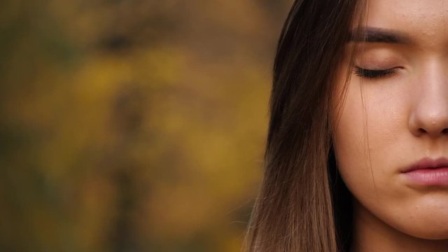Close up of the half female face with long brown hair with close eyes and then open, outdoors in autumn or summer park. Copy space