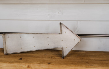 The arrow on wooden shelf indicates the direction on the white wooden wall.
