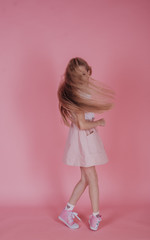 Motion, freedom and people concept - teenage girl dancing over pink background. Long blond hair hiding face.