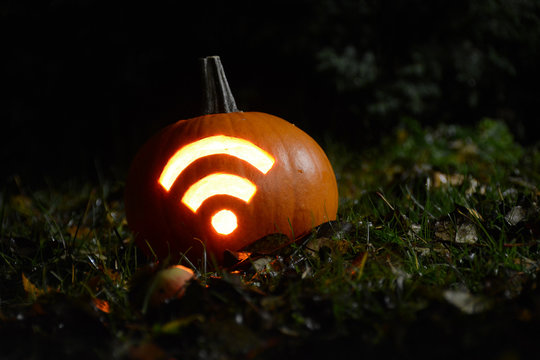 Closeup photo of pumpkin with carved Wi-Fi signal during Halloween night. Shot in garden with fallen apples, grass and leaves during autumn time.
