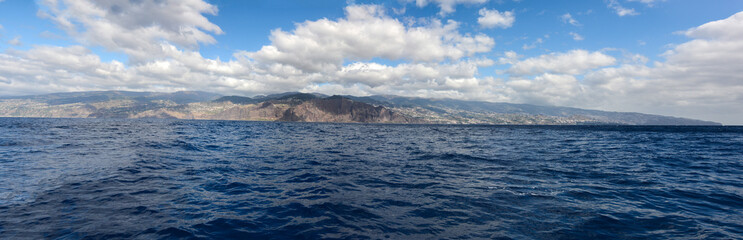 Wide panoramic view of Madeira island. High buildings and town on an island with blue skies and clouds in background