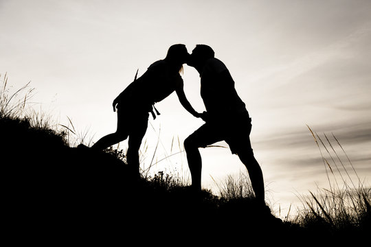 una pareja (chico y chica jovenes) d&aacute;ndose un beso en el monte a contraluz (silueta) durante la puesta del sol. monta&ntilde;eros