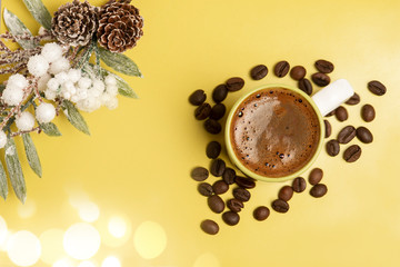 Beautiful christmas decoration. Christmas tree branch with pine cone. Fresh arromatic black coffee cup, and coffee beans, on the yellow background.