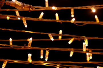Naklejka premium Part of Christmas decorative yellow, golden, white flashing lights, close up. Detail of New Year and Christmas decorations, string rice lights bulbs. Ornaments to christmas celebration, holiday scene.