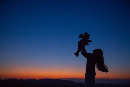 Happy child and parents walk at sunset. Dad hugs daughter and whirls in flight. Silhouette of a family walking in the sun. Mom dad and baby. The concept of a happy family. Family lifestyle.