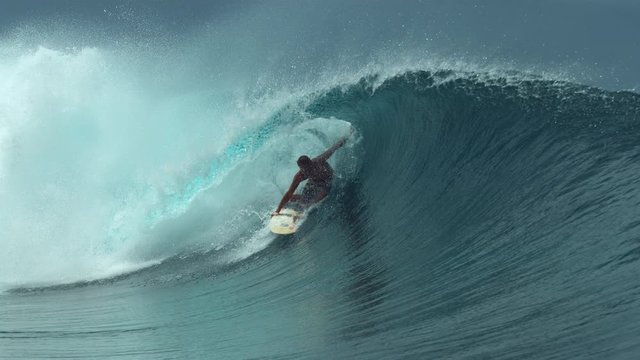 SLOW MOTION, CLOSE UP: Awesome male surfer rides a beautiful emerald barrel wave on a perfect day for surfing in sunny Tahiti. Young surfboarder enjoying catching perfect waves in French Polynesia.