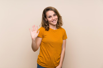 Young blonde girl over isolated background saluting with hand with happy expression