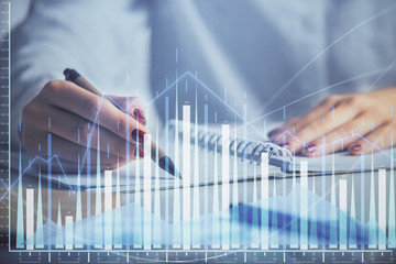 Double exposure of woman's hands making notes with forex graph hologram. Concept stock market...