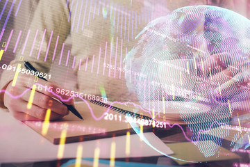 Forex chart hologram on hand taking notes background. Concept of analysis. Double exposure