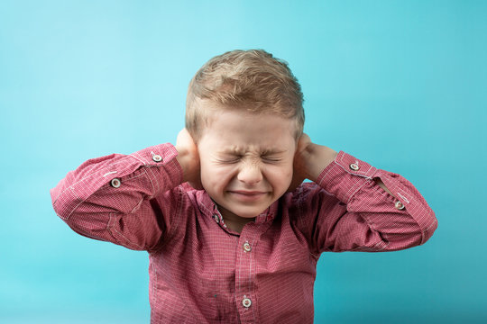 Boy Covered His Ears With His Hands. A Child In A Red Shirt On A Blue Background. The Disobedience Of The Child. Not Listening To Parents