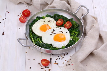Fried eggs in a pan with tomatoes and green spinach