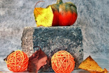 lightly decorated concrete stone with pumpkin, bast balls and autumn foliage