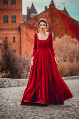 Beautiful girl in a burgundy red dress walking near  old castle on a background of autumn grape...