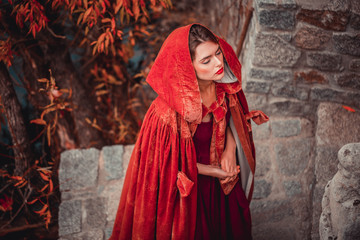 Naklejka premium Beautiful girl in a burgundy coat and red dress on a background of autumn grape leaves in the park, October