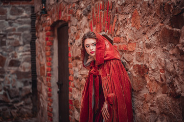 Beautiful girl in a burgundy coat and red dress on a background of autumn grape leaves in the park, October