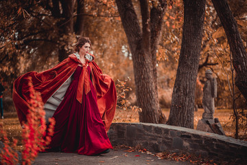 Naklejka premium Beautiful girl in a burgundy coat and red dress walking in the park, October