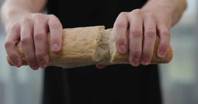 Slow motion man hands tear hot ciabatta bread indoors