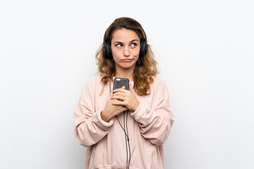 Fototapeta premium Young blonde woman using the mobile with headphones and thinking