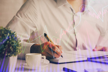 Double exposure of man's hands writing notes of stock market with forex chart.