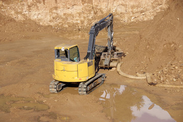 An excavator at the bottom of a construction excavation site after the rain