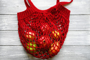 knitted red mesh shopping bag full fruit apples and pomegranate on white wooden background