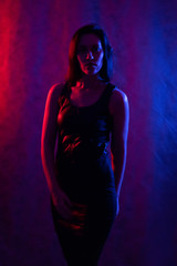 Studio portrait of a beautiful girl in a black dress. in the light of red and blue lamps.