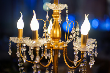 Luxury golden electrical chandelier lamp which is using to decorate the ceremony event or happy new year party in hotel's ballroom. Selective focus at the center pole.