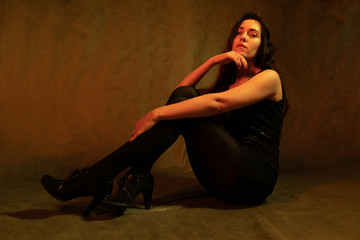 Studio portrait of a beautiful girl in a black dress sitting on the floor