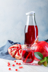 Bottle with pomegranate juice and a glass, ripe pomegranate, whole and peeled on a white wooden background