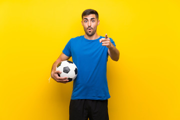 Young handsome football player man over isolated yellow wall surprised and pointing front