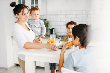 Young woman mom with baby girl on hands cooking breakfast on bright kitchen at home, large happy family